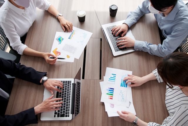 円卓を囲んで日米ビジネスパーソンが会議を行っている。資料が机上に広げられている