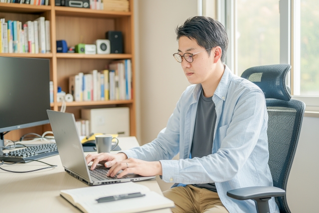 書類と資料が並んだデスクで担当者が作業をしている。オフィス環境